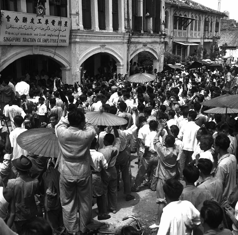Image shows a large group of people standing along a street. 